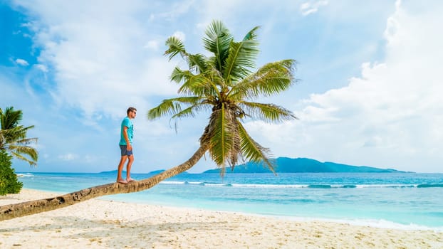 Young men relaxing at a palm tree on a tropical white beach at the La Digue Seychelles Islands.