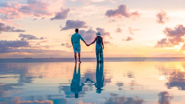 Young men and women watching the sunset with reflection in the infinity swimming pool at Saint Lucia Caribbean, a couple at infinity pool during sunset with a colorful sunset in the ocean