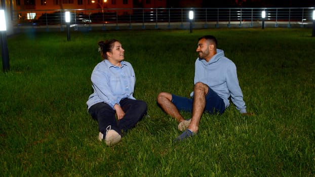 Romantic date within beautiful natural environment, green, juicy lawn. Media. Beautiful, young couple sitting on lush meadow and enjoying evening together