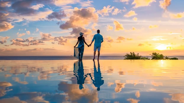 Young men and women watching the sunset with reflection in the infinity swimming pool at Saint Lucia Caribbean, couple at infinity pool during sunset