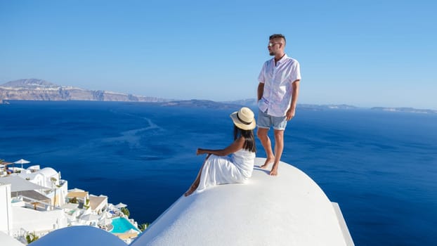A couple watching the sunset on top of a dome of a white hotel on vacation in Santorini Greece, Diverse multiracial couple on summer holidays in Europe