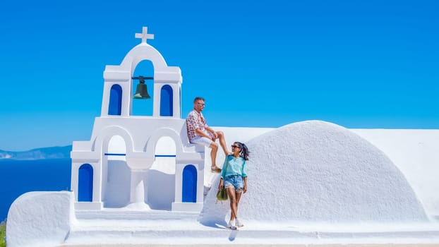 A couple of men and woman watching the sunset on vacation in Santorini Greece, men and women visit the Greek village of Oia Santorini. Diverse multiracial couple on summer holidays in Europe