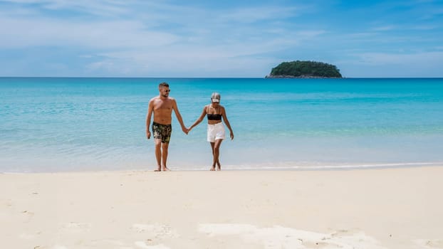 Mature couple walking on the beach of Kata Phuket Thailand during vacation, happy men and woman on vacation holidays in Thailand walking by the ocean of Kata Beach Phuket