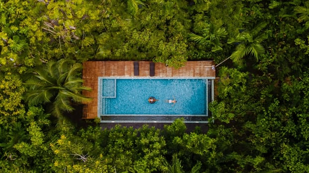 aerial drone view swimming pool in the jungle of Krabi Thailand, aerial view with a drone above a swimming pool in the rainforest of Thailand. couple of men and women in pool during vacation holiday