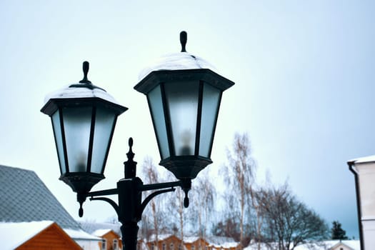 Street lamp close-up during the day against the backdrop of a winter village