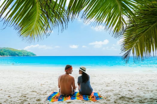 Couple relaxing under a palm tree on a white tropical beach Anse Lazio Beach Praslin Seychelles, Tropical Seychelles Islands on a sunny day during summer vacation