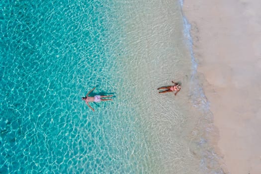 drone view of a man and woman swimming in the blue turqouse colored ocean of Koh Kradan island in Thailand. top view from above at the beach of Koh Kradan Trat Thailand