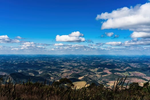 Endless rolling hills covered in grass, stretching to the horizon, under a bright blue sky filled with fluffy white clouds. No man-made structures in sight.