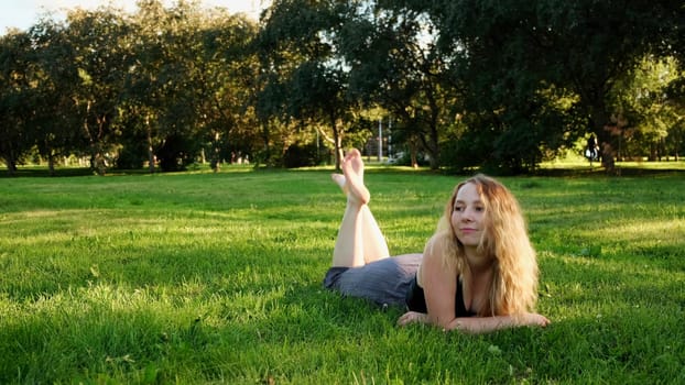 A cheerful woman in a clearing. Concept. A beautiful woman with long curly hair lying on the grass swinging her legs and laughing. High quality 4k footage