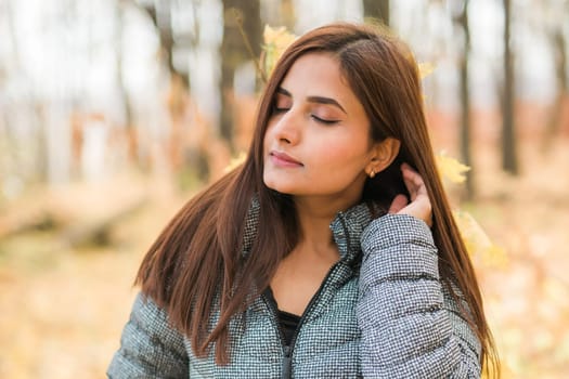 Close-up portrait of a young beautiful confident Indian Asian woman in fall outdoor. Happy and natural smiling female. Generation z and gen z youth