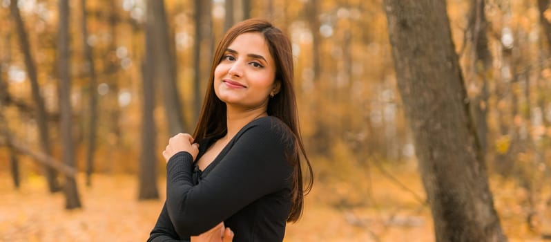 Close-up portrait of a young beautiful confident Indian Asian woman in fall outdoor. Happy and natural smiling female. Generation z and gen z youth