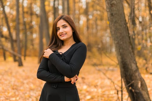 Close-up portrait of a young beautiful confident Indian Asian woman in fall outdoor. Happy and natural smiling female. Generation z and gen z youth