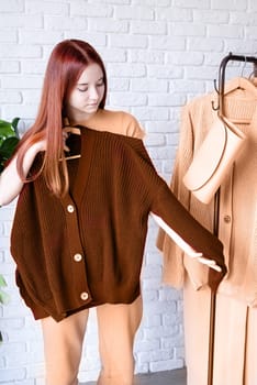 Color of the year 2024: Peach Fuzz. beautiful young woman in beige coat standing in front of hanger rack and choosing outfit dressing. Selection of a wardrobe, stylist, shopping. Clothes designing