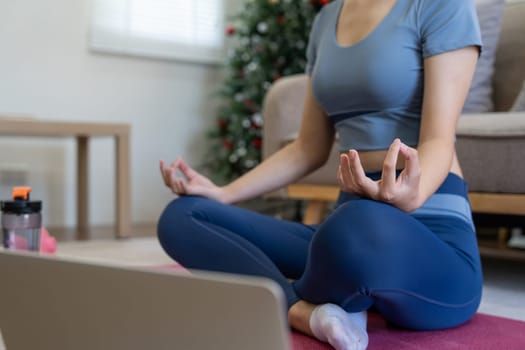 Young Asian woman meditating with trainer online on laptop at home.