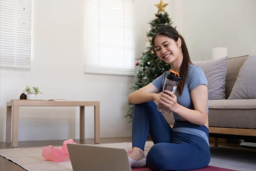 Young Asian woman using laptop and drinking water while doing yoga exercise at home. relax time.