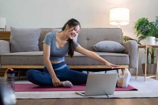 Young Asian sporty fitness woman coach do practice video online training yoga laptop in living room at home.