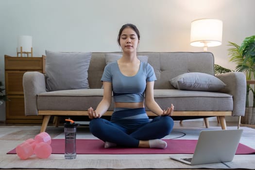 Young Asian woman meditating with trainer online on laptop at home.