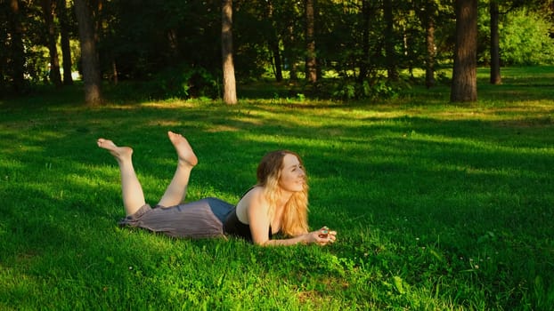 Beautiful young woman lying on grass in park in summer. Concept. Beautiful blonde woman is lying on grass and talking on sunny day. Attractive young woman is resting on summer green grass.