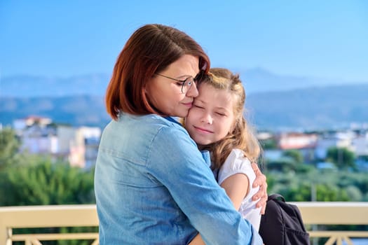 Mom hugging her preteen daughter. Girl schoolgirl with backpack hugging her mother on porch of house. Family, relationship, childhood, happiness, mother's day concept