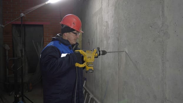 Builder in uniform drills hole in wall. Clip. Repairman makes hole with drill. Builder with drill makes hole in new room.