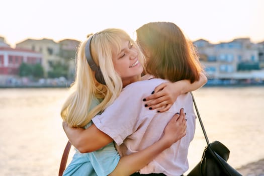 Happy mom and teenage daughter hugging together. Family mother and daughter outdoor, on sunset summer sea embankment. Mother's day, childhood, friendship, love, parent teenager concept