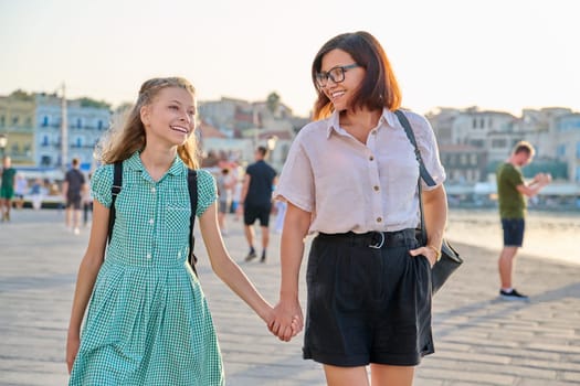 Mom and daughter child with a backpack holding hands together. Woman parent walking with child in city, outdoor. Generation, relationship, lifestyle, communication, family concept