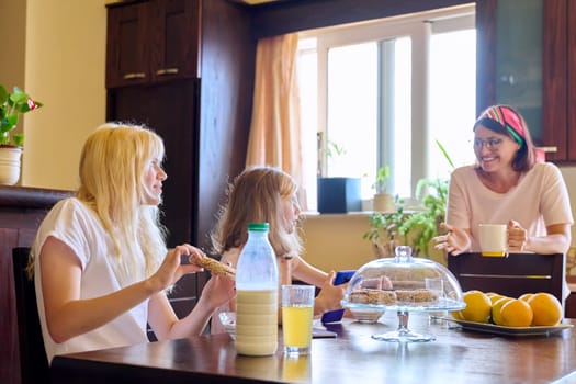 Children two sisters eating at home in the kitchen, teenage and preteen girls having breakfast together, mother cooking. Family, people, children, food, lifestyle concept