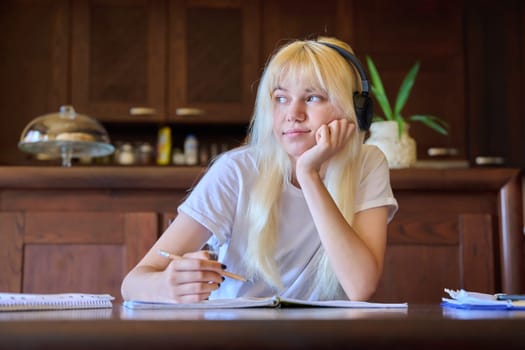 Portrait of a teenage student girl in headphones studying at home, sitting at the table. Technology, high school, college, education, knowledge, e-learning concept