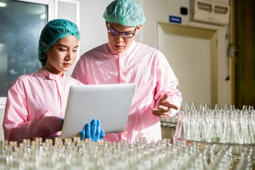 Engineers inspect product bottles on a conveyor belt within a beverage factory line. Quality control and thorough inspection conducted by professionals using a laptop for analysis.