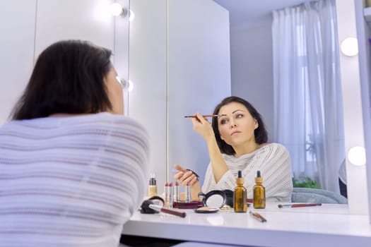 Beautiful middle aged woman doing makeup in front of a mirror. Cosmetics, beauty, make-up, face care, skin care, women 40s age concept