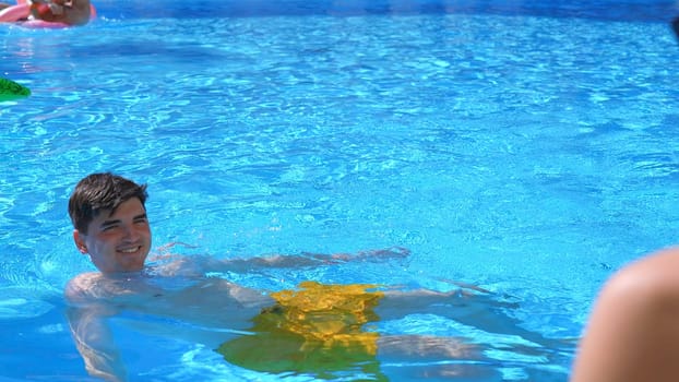 Young happy man swimming in the swimming pool in front of his girlfriend. Clip. Concept of travelling and vacation