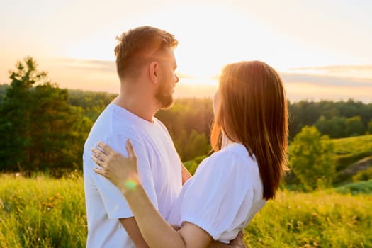 Outdoor portrait of adult happy loving hugging couple. Smiling 40s man and woman in white clothes, together at sunset, scenic natural landscape background. Relationship, love, happiness, family people