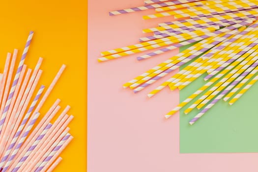 Drinking paper straws on yellow background with copy space. Top view of colored paper disposable eco-friendly straws for summer cocktails.