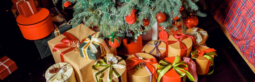 Christmas background with red gift boxes decorated with golden ribbon on floor and child toys under Christmas tree, copy space. Winter holidays concept