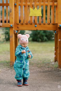 Little laughing girl blowing soap bubbles while standing on the playground. High quality photo