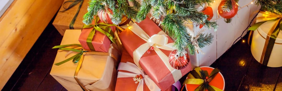 Christmas background with red gift boxes decorated with golden ribbon on floor and child toys under Christmas tree, copy space. Winter holidays concept