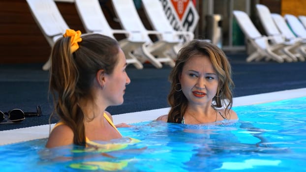 Attractive women during summer vacation talking in a swimming pool. Clip. Beautiful ladies resting together in blue water