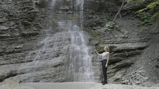 Shooting a waterfall using a camera device. Action. Beautiful nature with mountains on which a young beautiful girl shoots water drops falling from the mountains on camera