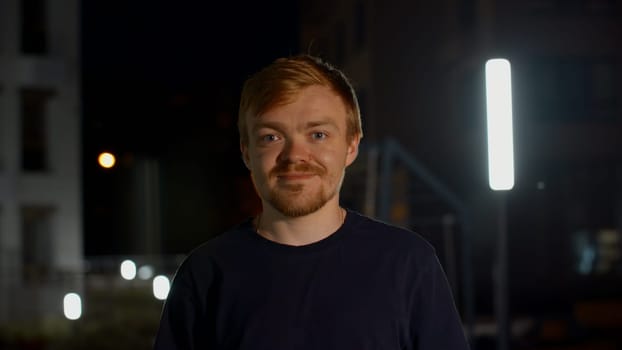 A handsome man posing on the street. Media. Night shooting of a portrait of a man with a beard in a hat. High quality 4k footage