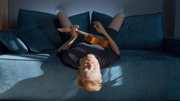 A man resting lying down. Media. A handsome man lying on a bed and playing the ukulele under the rays of the sun in a bright room