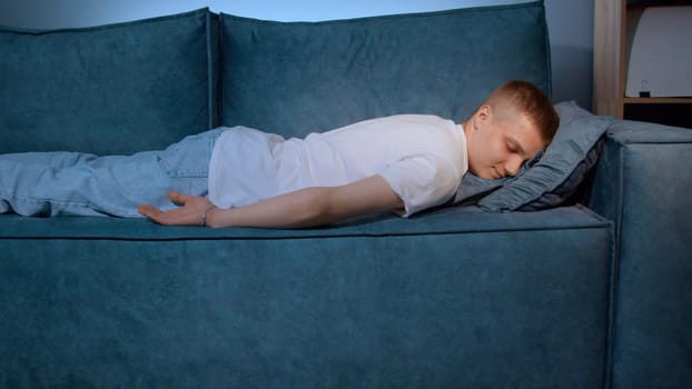 Tired boy slumping on couch feeling listless. Media. Feeling depressed, lack of motivation, sadness, boredom. Exhausted, he collapses on the couch from stress