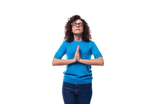 portrait of a young woman with curly hair dressed in a blue t-shirt meditating on a white background.