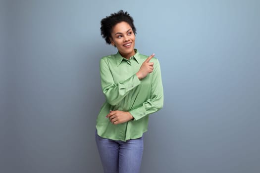 cute young brunette hispanic woman dressed in a green blouse points with her hand on the background with copy space. people lifestyle concept.