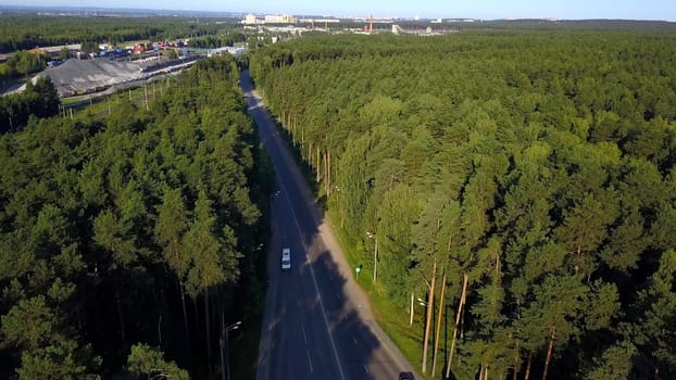 Aerial view of cars travelling in beautiful forested terrain. Clip. Vehicles driving on an asphalt road with a beautiful landscape