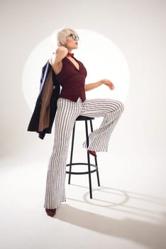 studio photo of a sexy girl in glasses and a suit on a bar stool on a light background