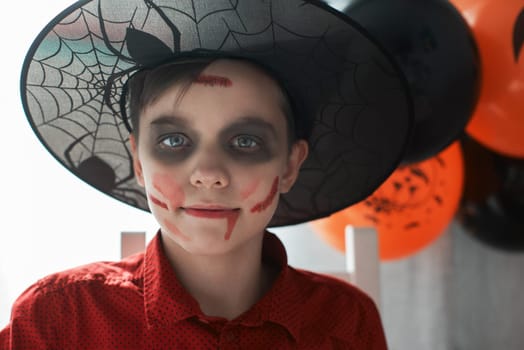 Happy teen boy in costume preparing for the Halloween celebration drawing a pumpkin. Halloween carnival or masquerade concept