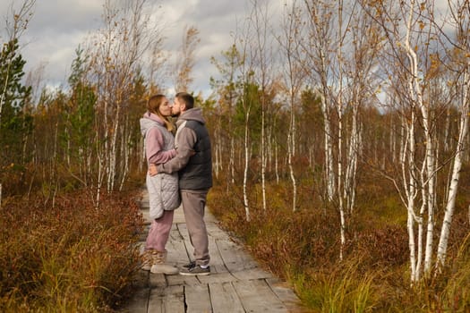 Tourists with backpacks kiss a wooden path in a swamp in Yelnya, Belarus.