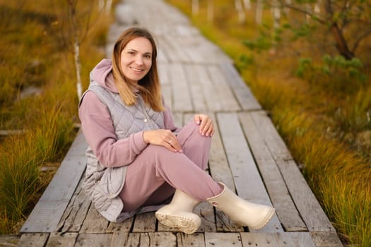 A woman sits on a wooden path in a swamp in Yelnya, Belarus.
