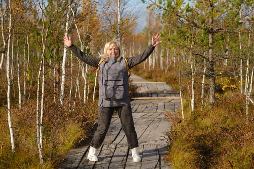 A happy woman with a backpack jumps on a wooden path in a swamp in Yelnya, Belarus.