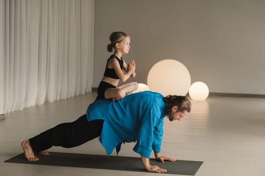 a child in the lotus position sits on the back of a yoga coach during training.